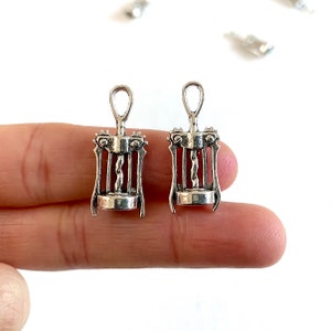 K&ouml;nnte beinhalten: Zwei silberfarbene Korkenzieher-Anh&auml;nger aus Metall. Die Anh&auml;nger sind mit einem Korkenzieher-Design verziert und haben oben eine &Ouml;se zum Anbringen an einer Halskette oder einem Armband.
