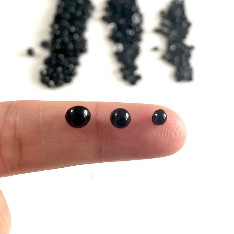 May include: Three black plastic safety eyes of different sizes. The eyes are round and have a glossy finish.