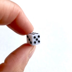 May include: A white plastic dice with black dots showing the number six.