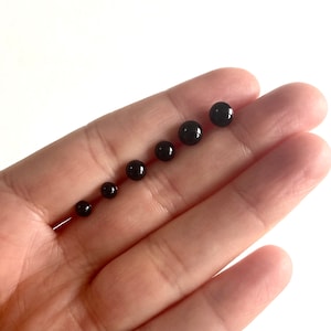 May include: A set of six black round beads of varying sizes, arranged in order from smallest to largest, on a hand.