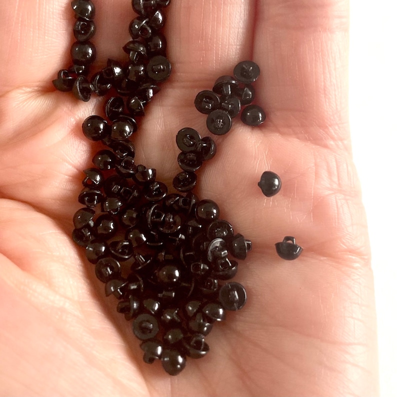 May include: A large pile of black plastic buttons with a few smaller buttons scattered around them.