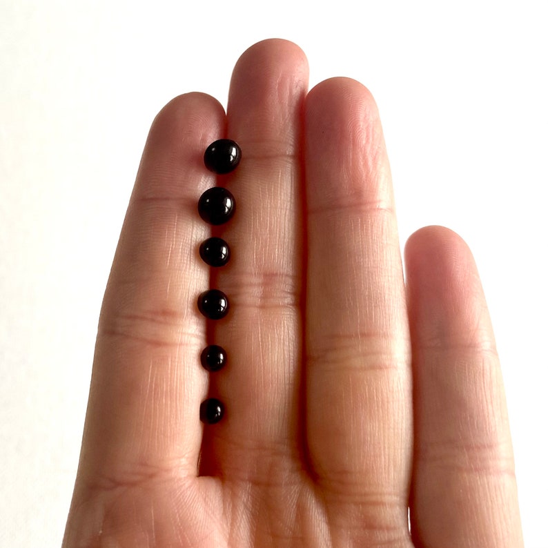 May include: A set of seven black round beads of varying sizes, displayed on a hand.