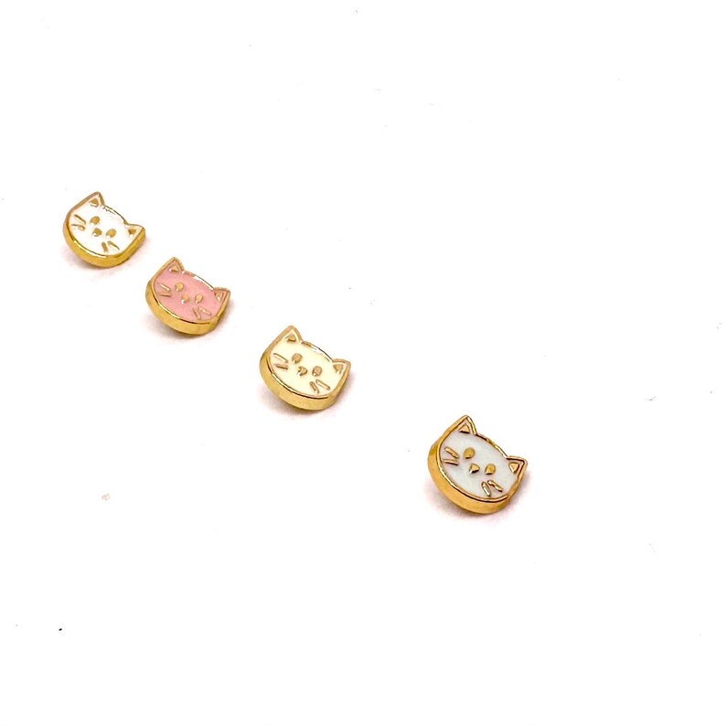 May include: Four gold-colored cat face buttons with white and pink enamel. The buttons are arranged in a row from left to right.