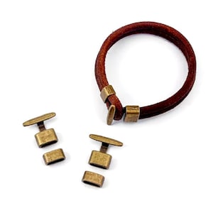 May include: Two sets of antique gold-toned metal clasps for leather bracelets. Each clasp has a rectangular buckle and a small bar that slides through the buckle. The clasps are on a white background.