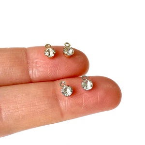 May include: Three gold-toned metal charms with clear round rhinestones. The charms have a loop at the top for attaching to jewelry or other crafts.