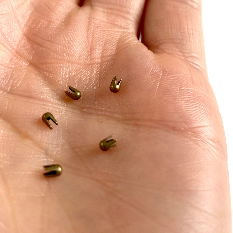 May include: Five gold-colored metal rivets with a pointed tip and a rounded head. The rivets are arranged in a scattered pattern on a light-colored surface.