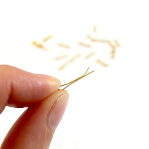 May include: A close-up of a gold bobby pin held in a hand. The bobby pin is a simple, straight design with a slight bend at the end.