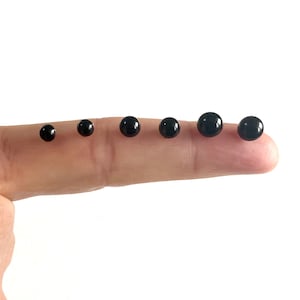 May include: A set of six black round beads of varying sizes, arranged in order from smallest to largest on a finger.