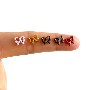 Könnte beinhalten: Fünf kleine Metall-Schleifen-Anhänger in verschiedenen Farben: rosa, gold, bronze und rot. Die Anhänger werden auf einem Finger gezeigt.