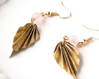 May include: A pair of gold-colored leaf earrings with pink beads. The earrings have a delicate, folded leaf design and gold-tone ear wires. The earrings are displayed on a white surface.