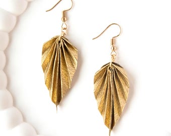 May include: A pair of gold-colored leaf-shaped earrings. The earrings have a detailed, folded design, with a hook closure. The earrings are displayed on a white background.