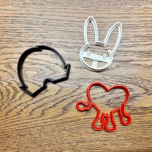 May include: Three cookie cutters: a black bunny, a white bunny, and a red blob.