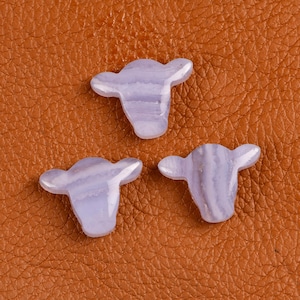 Puede incluir: Tres cabujones de ágata azul claro con forma de vaca, con bandas blancas y azules. Los cabujones están sobre un fondo marrón. Estas piezas de piedras preciosas son adecuadas para la fabricación de joyas o proyectos de artesanía.