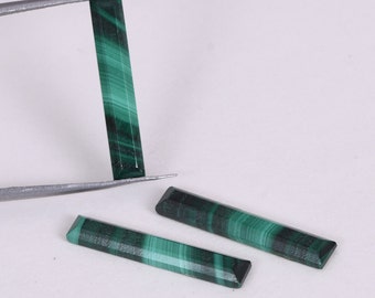 May include: Three green malachite gemstone cabochons in a rectangular shape. The cabochons are smooth and polished with a green and black marbled pattern.