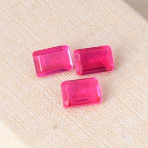May include: Three pink rectangular gemstones with a faceted cut.