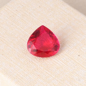 May include: A teardrop-shaped, faceted gemstone with a deep red color. The gemstone is set against a white background.