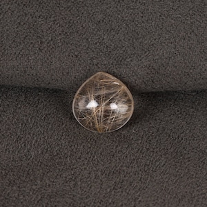 May include: A clear quartz crystal with inclusions of brown hair-like fibers. The crystal is round and has a smooth, polished surface.