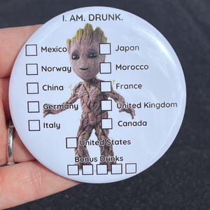May include: A white round button with a cartoon character, a green alien with a brown body, and a checklist of countries. The text "I. AM. DRUNK." is at the top of the button. The checklist includes the following countries: Mexico, Japan, Norway, Morocco, China, France, Germany, United Kingdom, Italy, Canada, United States, and Bonus Drinks.
