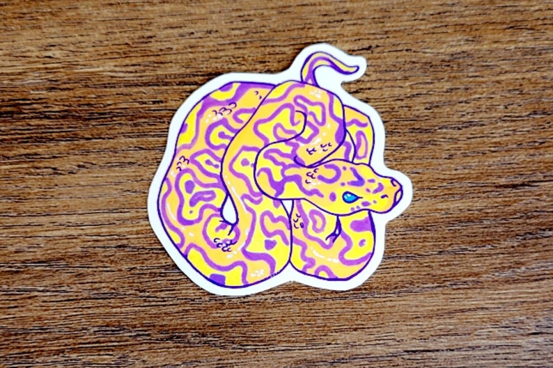 May include: A yellow and purple snake sticker with a blue eye. The snake is curled up in a coil.