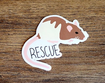 May include: A sticker featuring a cartoon rat with brown and white fur, a pink tail, and the word "RESCUE" in black letters. The sticker is on a wooden surface.