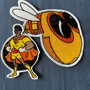 May include: Two embroidered patches, one featuring a superhero in a yellow and orange costume and the other a yellow and orange bee with black eyes.