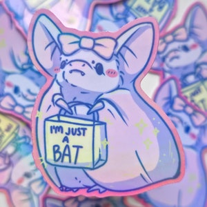 May include: A collection of holographic stickers featuring a cute cartoon bat with a pink bow and a shopping bag. The bag reads "I'M JUST A BAT". The stickers have a pastel color scheme with pink, purple, and blue hues.