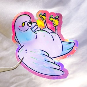 以下が含まれることがあります： ローラースケートを履いた紫色の鳩のホログラフィックステッカー。鳩はピンクの頬と黄色の目をしています。ローラースケートは黄色と緑色です。