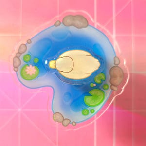 May include: A whimsical, transparent sticker featuring a pond scene. The sticker shows a blue pond with a yellow duck floating on the water. Lily pads, a pink flower, and rocks surround the pond. The background is a pink, tiled pattern.