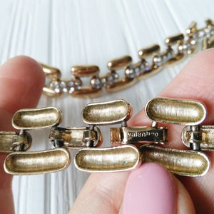May include: Gold-toned chain link bracelet with a textured finish. The bracelet features a clasp with the brand name "Valentino" engraved. Some links are adorned with small, clear crystals, adding sparkle to the jewelry.