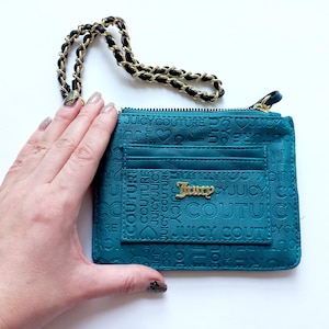 May include: Teal wallet with a gold-tone chain strap. The wallet features the word "Juicy" in gold lettering and embossed text of "Juicy Couture". The wallet has a zip closure and card slots.