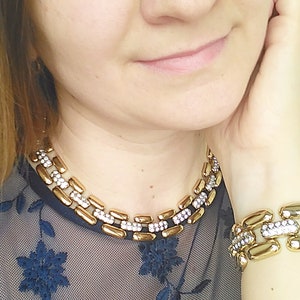 May include: Gold-toned necklace and bracelet set. The jewelry features rectangular links with a central row of clear crystals. The necklace sits around the neck, and the bracelet is on the wrist.