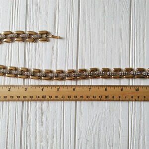 May include: A gold-toned necklace with rectangular links, each accented with a row of small, clear rhinestones. The necklace is approximately 12 inches long, as measured by a wooden ruler.