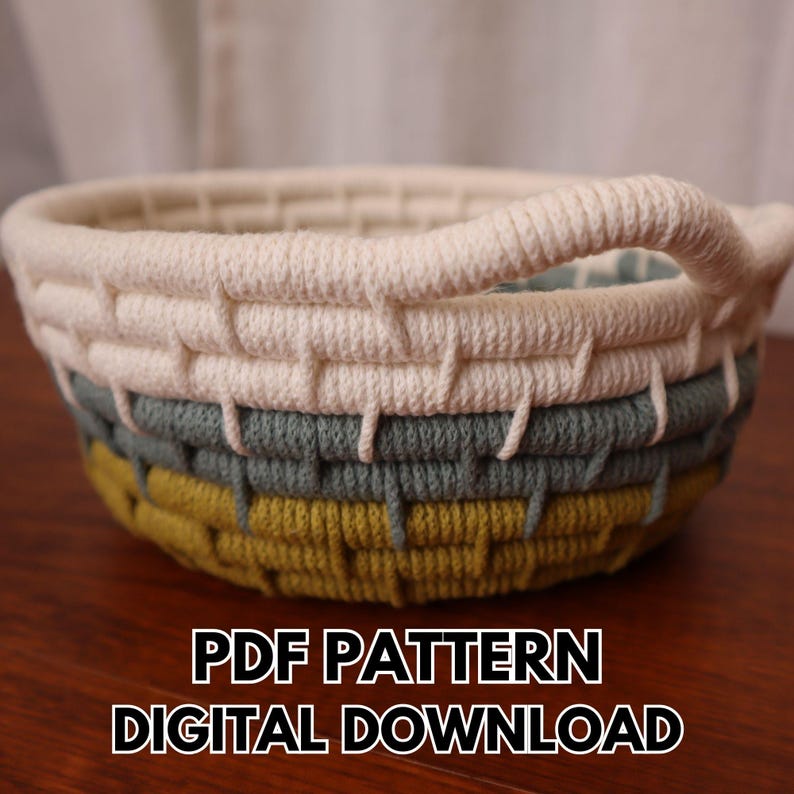 May include: A handmade, round basket with a woven design. The basket features a cream-colored top, a gray-green middle section, and a yellow-green base. It has a cream-colored handle. The text "PDF PATTERN DIGITAL DOWNLOAD" is at the bottom.