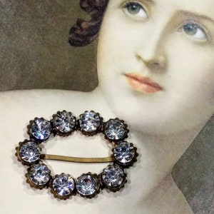Peut inclure: Une broche ovale vintage avec un sertissage en métal argenté et un cercle de strass transparents.