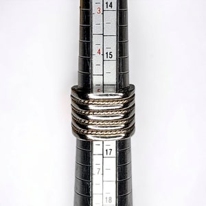 May include: A silver and gold ring with a braided design, measured on a ring sizer with markings from size 14 to 18.
