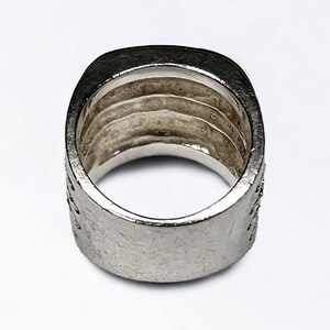 May include: A silver ring with a square band and a textured surface. The ring has a wide band and is designed to be worn on the finger.