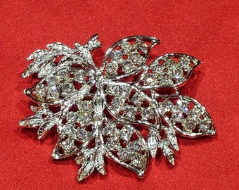 May include: A silver-toned brooch with a floral design, featuring intricate details and sparkling rhinestones.