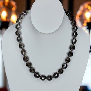 May include: A necklace made of dark grey faceted beads. The beads are round and have a slight sparkle to them.