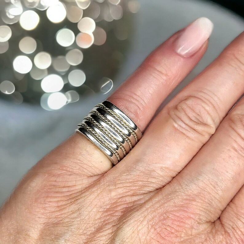 May include: A silver and gold ring with multiple bands. The ring is worn on a finger.