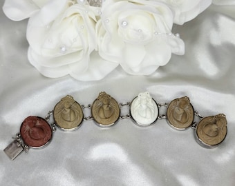 May include: A silver bracelet with six oval-shaped charms. Each charm features a cameo of a woman's face. The charms are connected by silver links. The bracelet has a red carnelian charm.