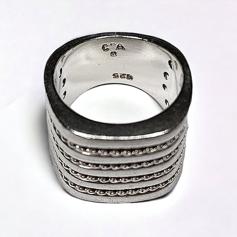 May include: Silver ring with a square band and a textured design. The ring is marked with "C.A. 925".