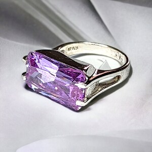 Peut inclure: Une bague en argent avec une grande pierre précieuse rectangulaire violette. La bague a un design simple et moderne et est marquée "MF125" sur la bande.
