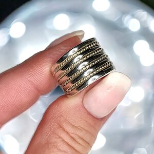 May include: A wide silver band ring with multiple gold bands wrapped around it. The ring has a rope-like texture.