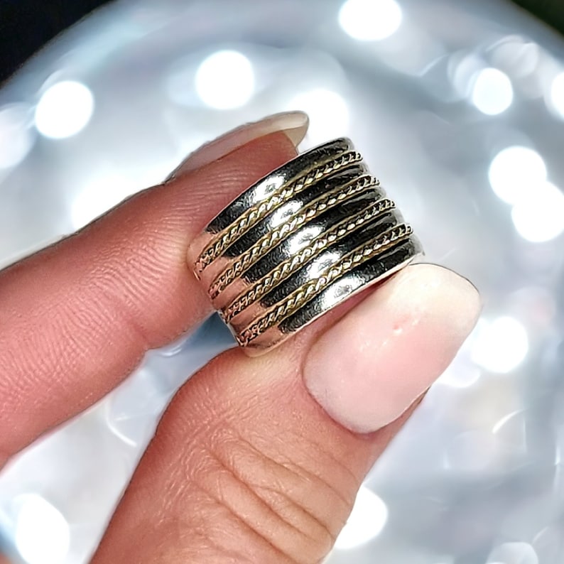 May include: A wide silver band ring with multiple gold bands wrapped around it. The ring has a rope-like texture.