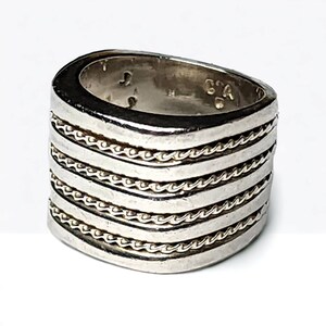 May include: A silver ring with five bands of rope-like detail. The ring is wide and has a rounded top.