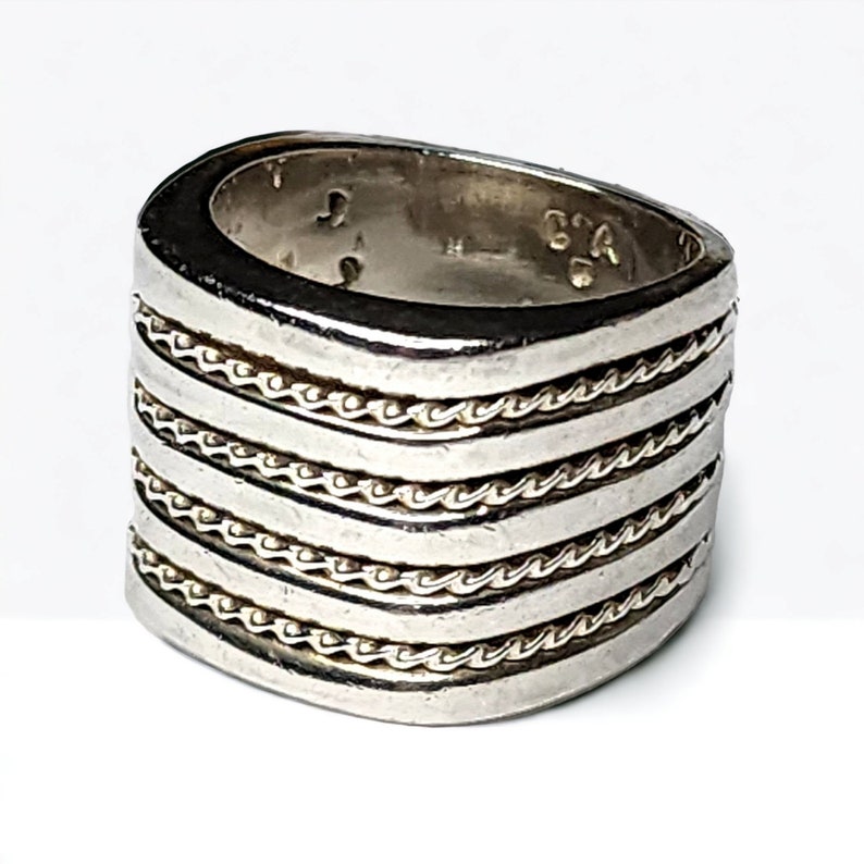 May include: A silver ring with five bands of rope-like detail. The ring is wide and has a rounded top.
