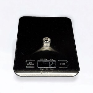 May include: A silver ring on a black digital scale that reads 12 grams. The scale has a black background with white text that reads "MAX=5000g d=1g", "Z/T ON/OFF", "Weight Milk Water", "ETEKCITY", and "UNIT".