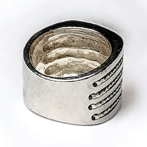 May include: A silver ring with a square band and a textured design. The band has a series of horizontal lines that create a rope-like effect.