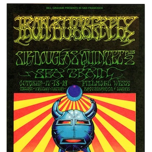 May include: A vintage concert poster for a performance by the  Frank Zappa  and the Mothers of Invention with the  Douglass Quintet  and  Sea Train. The poster features a psychedelic illustration of a robot with a large head and three pairs of legs, walking on a green field with a yellow and red striped background. The text on the poster reads "Bill Graham Presents in San Francisco" and "Fillmore West - Brotherhood of Light".