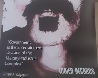 Könnte beinhalten: Schwarzweißes Poster mit einem Nahaufnahmeporträt von Frank Zappa mit dem Zitat "Government is the Entertainment Division of the Military-Industrial Complex" und dem Text "TOWER RECORDS".